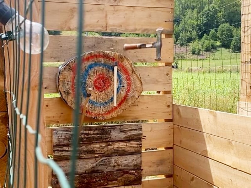 Hache plantée dans une cible en bois colorée rouge, bleu et blanc, dans un espace de lancer en bois en extérieur.