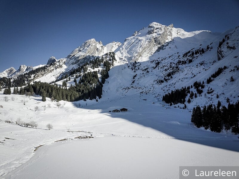 Paysage de montagne enneigé avec une vallée et des chalets au loin.