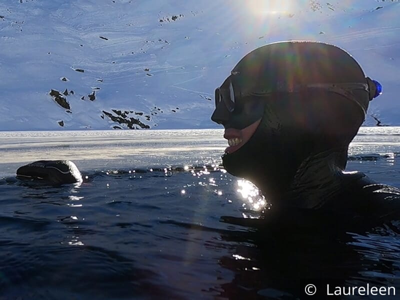 Plongeur souriant à la surface d'un lac gelé avec un décor montagneux.