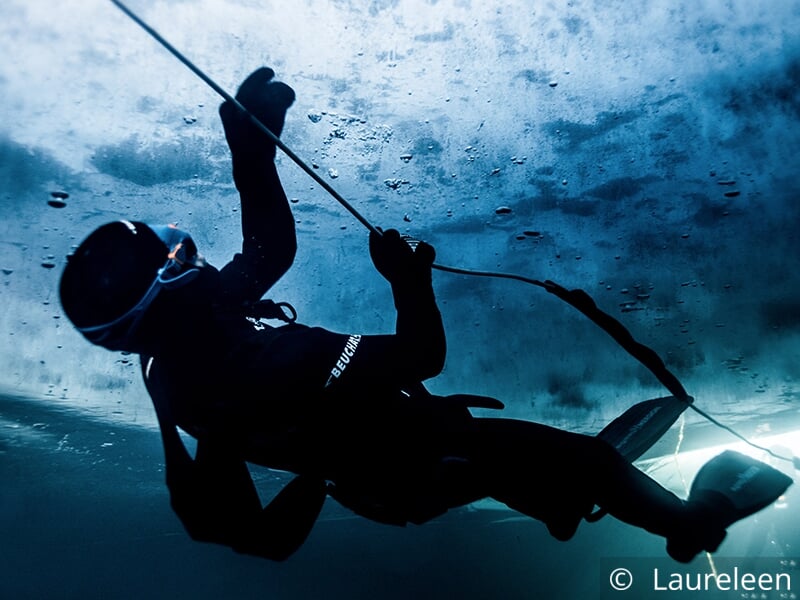 Plongeur sous la glace regardant vers la surface et tenant une corde.