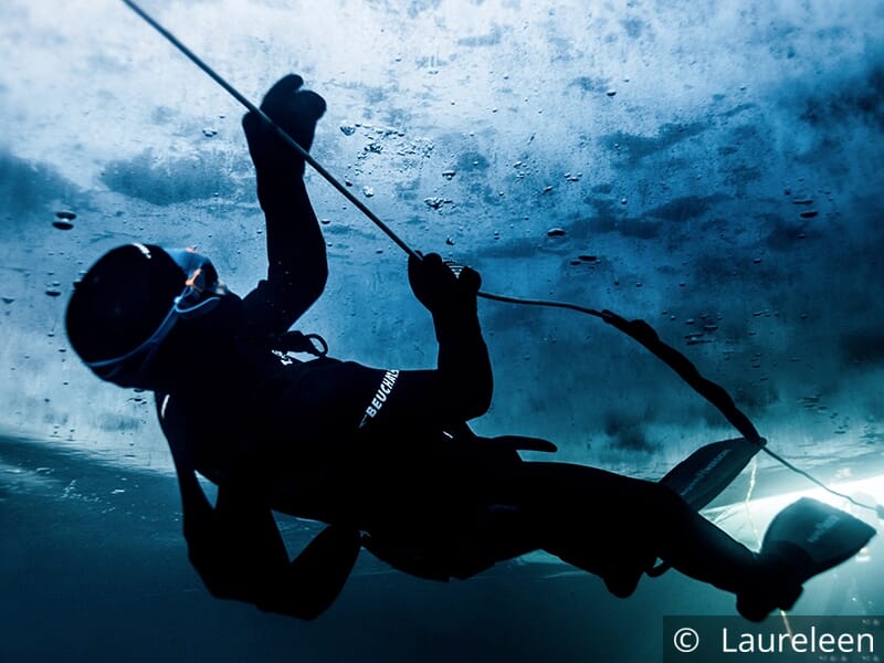 Plongeur sous la glace regardant vers la surface et tenant une corde.