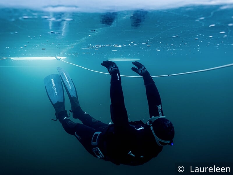 Plongeur en combinaison noire nageant sous la glace avec des palmes.