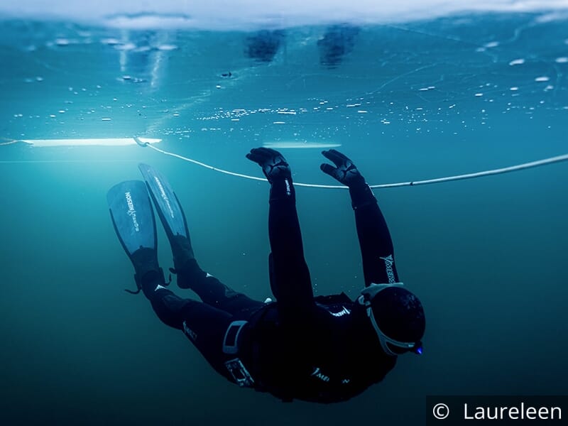 Plongeur en combinaison noire nageant sous la glace avec des palmes.