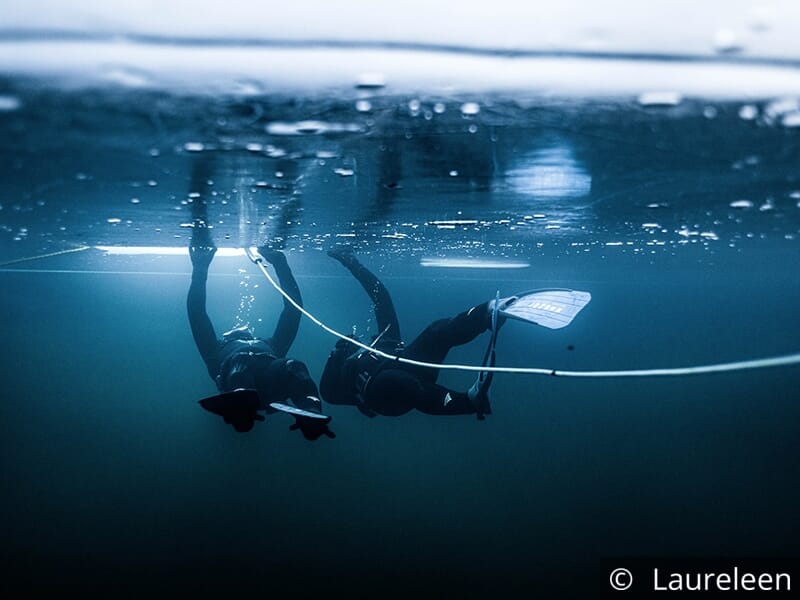 Deux plongeurs sous l'eau éclairés par des rayons de lumière à travers la glace.
