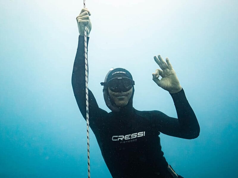 Trois plongeurs sous l'eau posant pour une photo en souriant, équipés de combinaisons et masques.