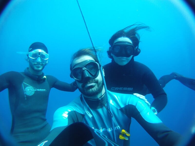 Plongeur descendant en apnée le long d'une corde dans une eau bleue avec la lumière du soleil au-dessus.