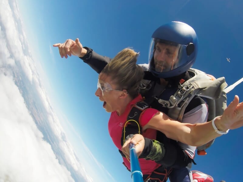 Femme en tandem avec un instructeur de parachutisme, pointant le ciel au-dessus des nuages