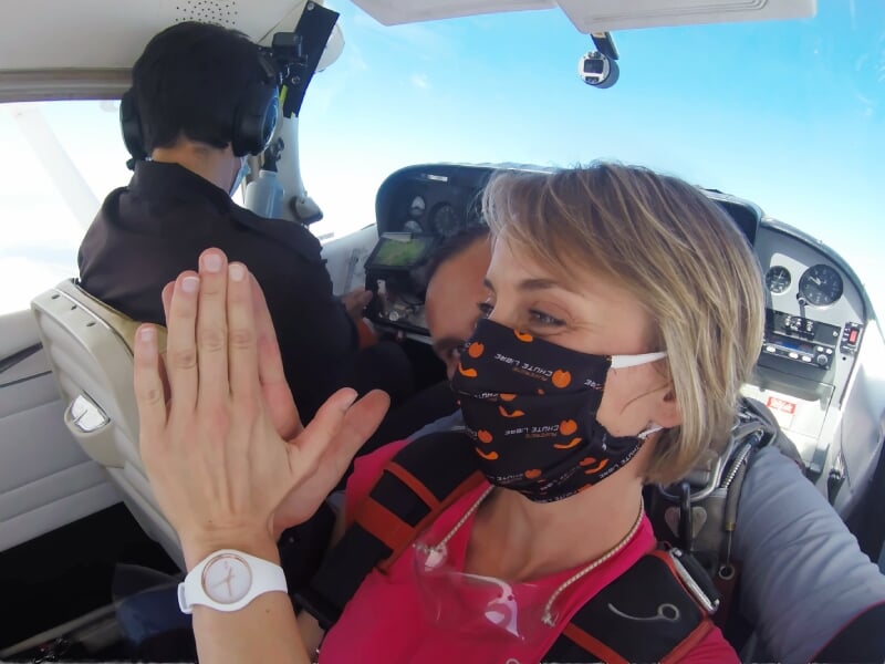 Femme en masque orange faisant un high-five dans un avion avant un saut en parachute