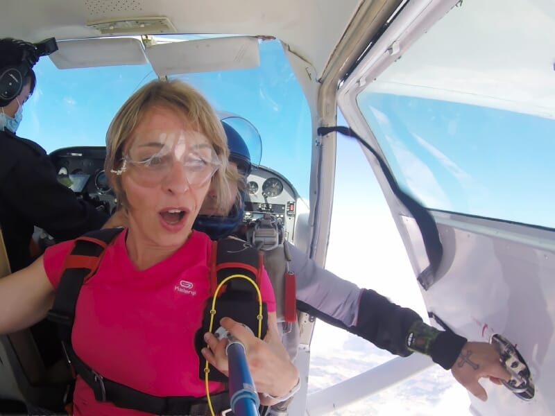 Femme en rose avec lunettes de protection à bord d'un avion, prête à sauter en parachute
