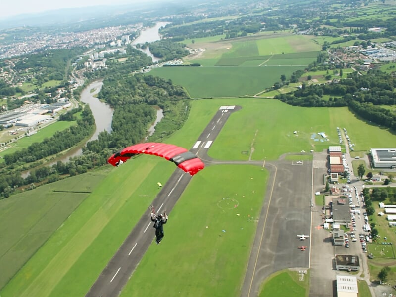 Parachutiste avec parachute rouge atterrissant sur une piste d'aéroport verdoyante