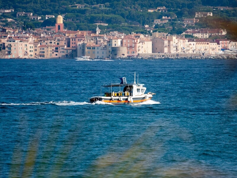 Petit bateau de pêche ou de plongée naviguant sur une mer calme avec la ville de Sainte-Maxime en arrière-plan.