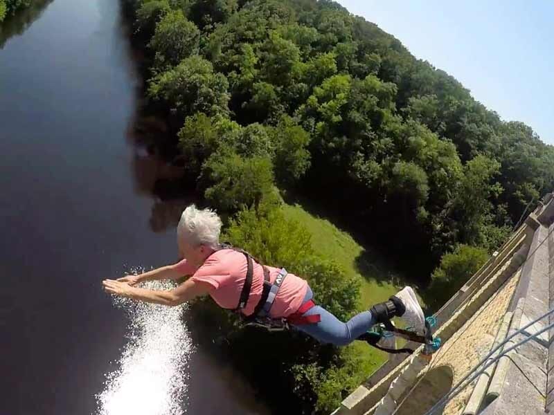 Personne en combinaison rose et bleue effectuant un saut à l'élastique depuis un pont au-dessus d'une rivière.