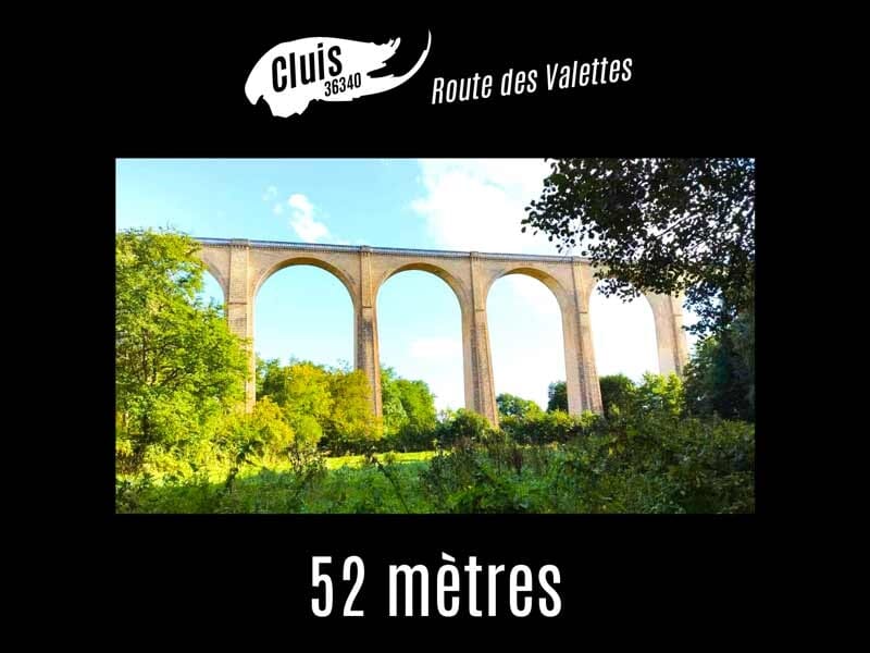 Viaduc de Cluis vu de loin avec ses grandes arches en pierre entouré de verdure sous un ciel bleu clair.