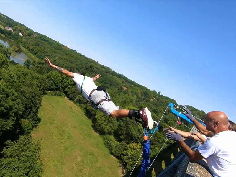 Homme en combinaison blanche se lançant dans un saut à l'élastique depuis un pont avec des assistants.
