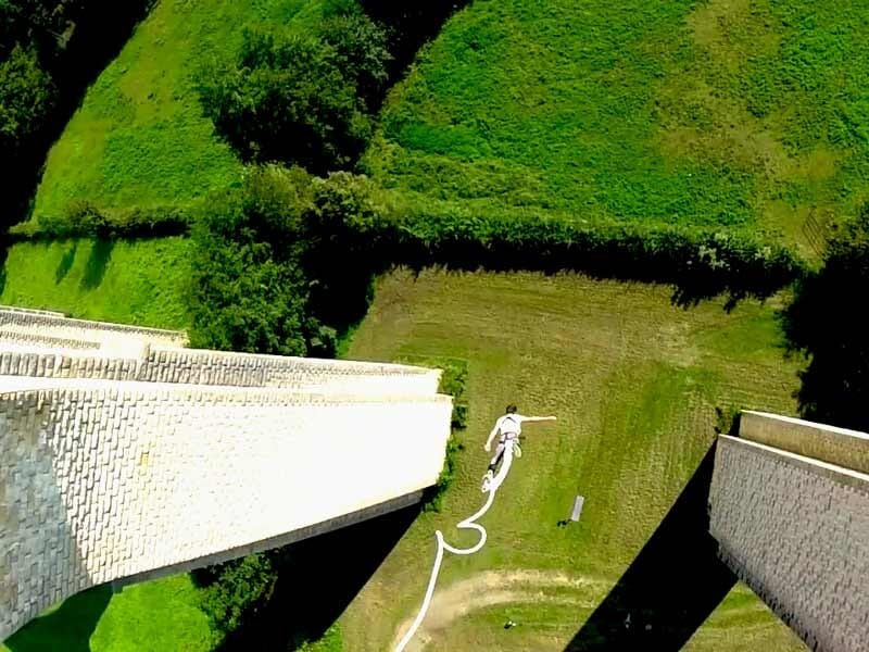 Vue plongeante d'un sauteur à l'élastique suspendu au bout de son élastique au-dessus d'un terrain vert.