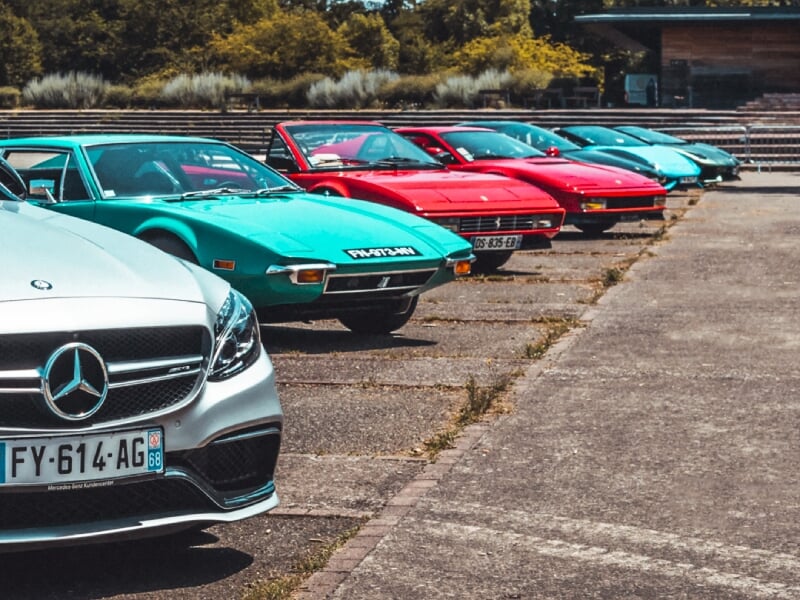 Vue en perspective d'une rangée de voitures de sport colorées garées sur un parking ensoleillé à Mulhouse.