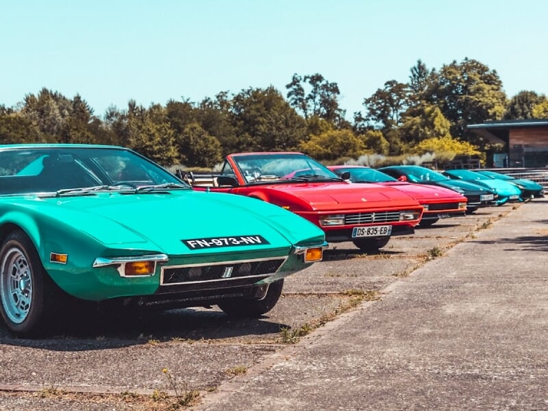 Alignement de voitures de sport anciennes et colorées sur un parking extérieur sous un ciel clair à Mulhouse.