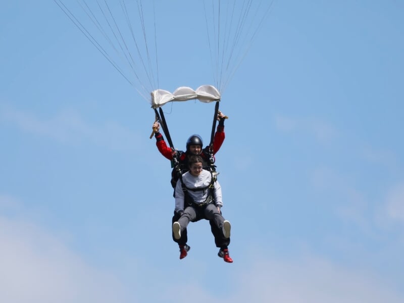 des parachutistes en tandem descendent en voile devant un ciel bleu dégagé