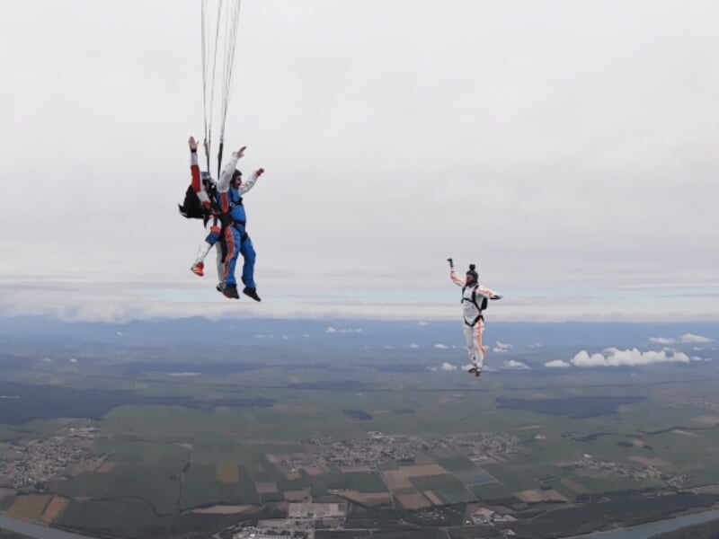 deux parachutistes tandem et un vidéoman extérieur en chute libre au-dessus d'un paysage brumeux
