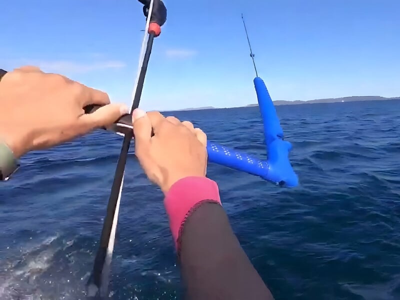 Vue rapprochée des mains d'une personne tenant la barre de contrôle d'un kite en mer avec un ciel bleu clair.