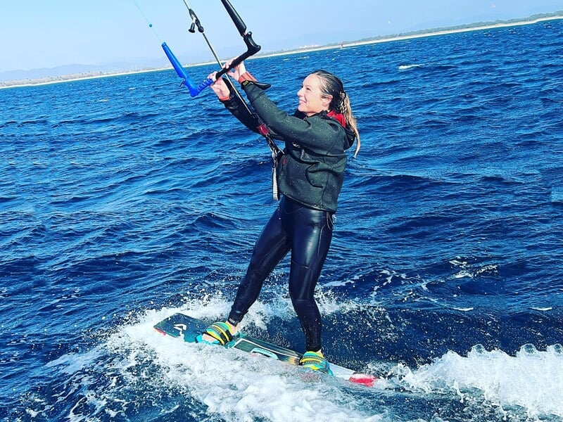 Femme en combinaison noire pratiquant le kitesurf sur une mer bleue avec des vagues et un ciel dégagé.