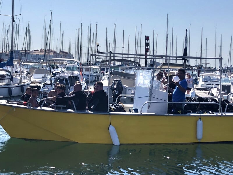 Un groupe de personnes sur un grand bateau jaune dans un port, entouré de nombreux voiliers et bateaux amarrés.