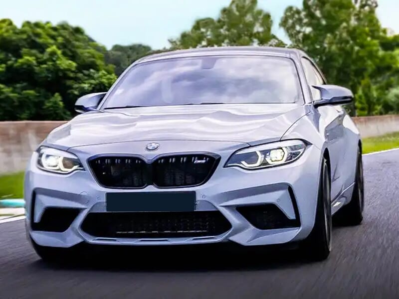 Vue frontale d'une BMW M2 blanche roulant sur une piste de circuit.