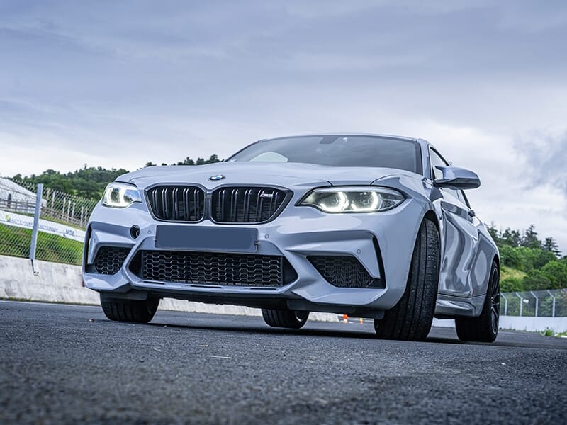 Vue rapprochée d'une BMW M2 blanche, prise sous un angle bas pour souligner son design agressif et sportif.