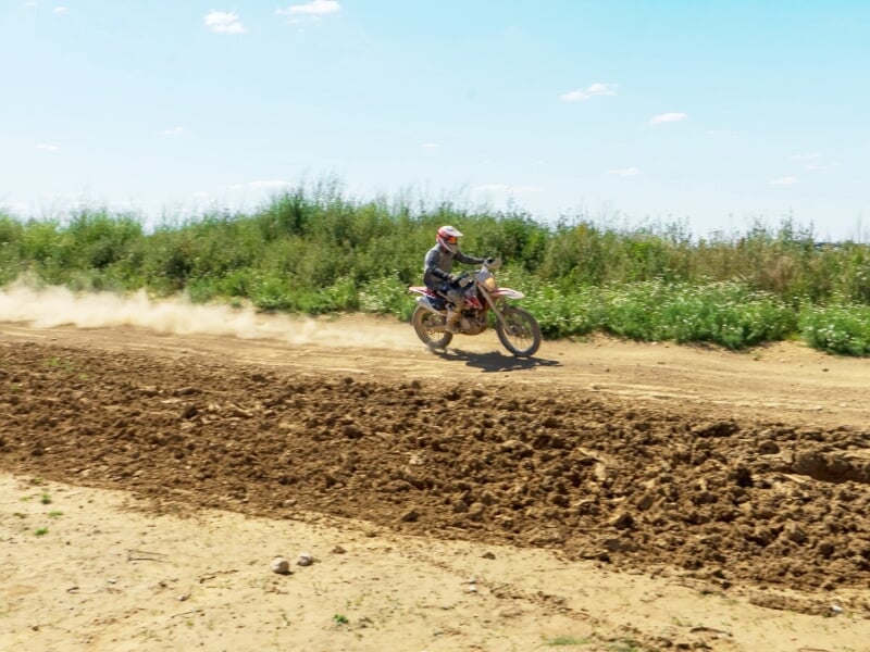 Motocross en action sur une piste de terre battue, soulevant de la poussière sous un ciel bleu clair.