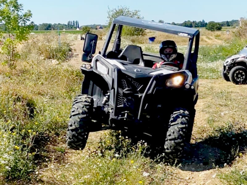Véhicule tout-terrain type buggy roulant sur un chemin étroit entouré de végétation en été.