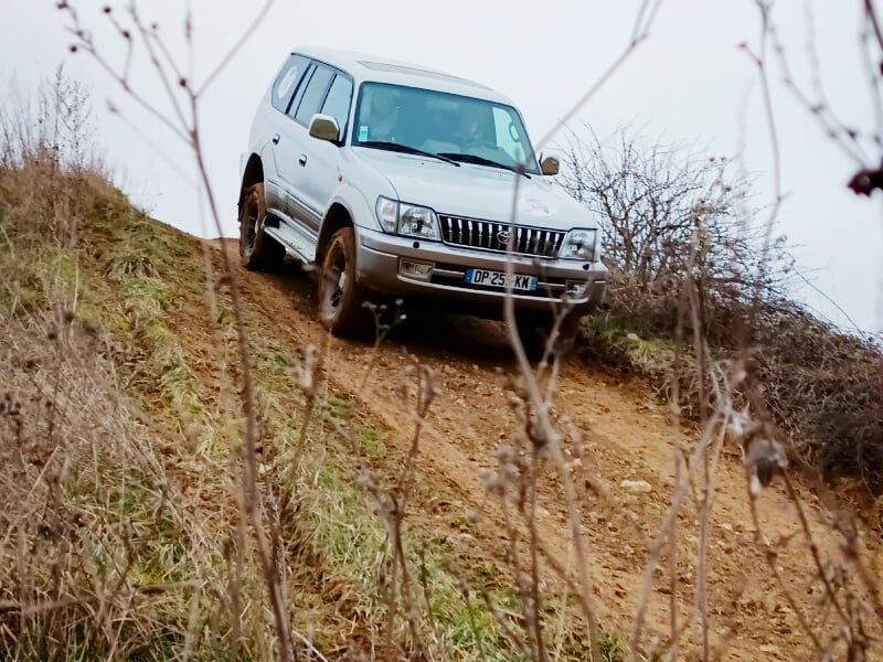 4x4 blanc descendant une pente boueuse dans un environnement naturel avec des arbres dépouillés.