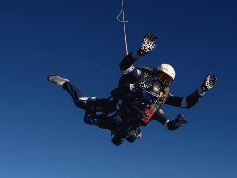 Parachutistes en chute libre, bras écartés, fixés à un parachute dorsal, ciel dégagé.