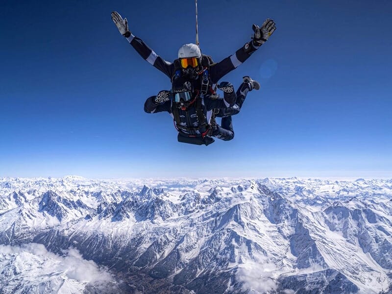 Vue de parachutistes en chute libre au-dessus des montagnes enneigées avec un large panorama.