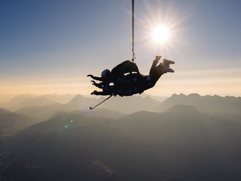 Parachutistes en vol avec le soleil couchant en arrière-plan, ombres des montagnes en contrebas.