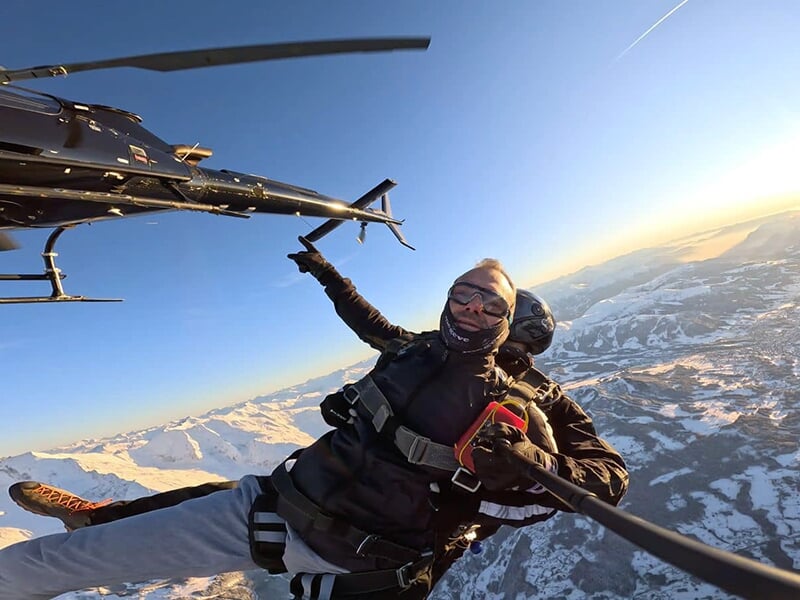 Parachutistes sautant depuis un hélicoptère en plein vol, avec vue sur les montagnes enneigée