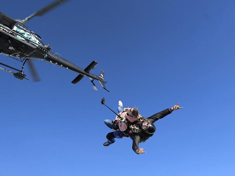 Deux parachutistes en chute libre, l'un en position inclinée, au-dessus d'un paysage alpin enneigé.