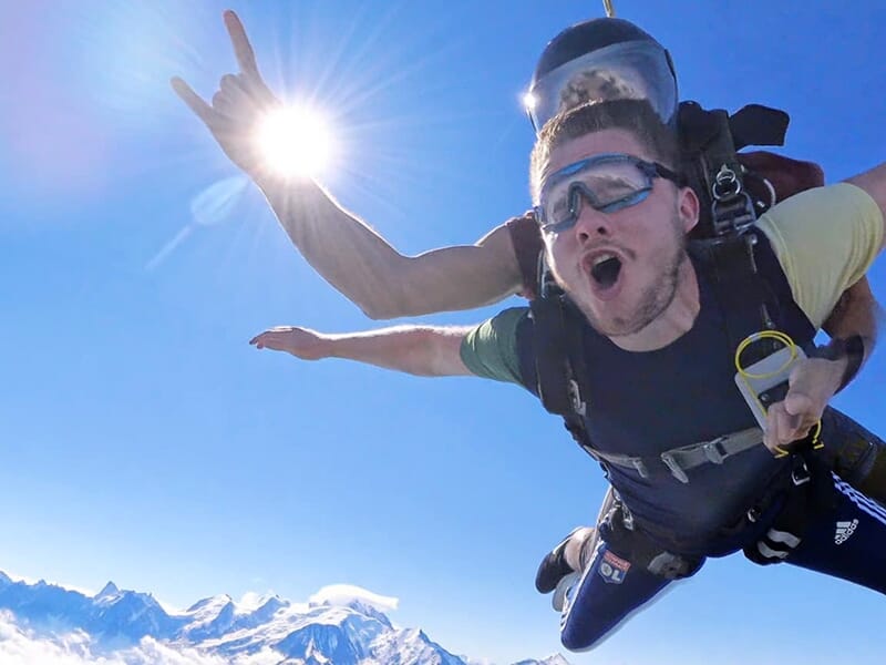 Parachutistes en chute libre avec un ciel bleu vif, le passager exprimant de la joie tandis que le soleil brille en arrière-plan.