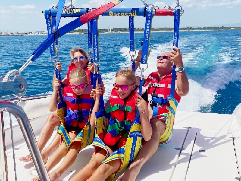 Trois personnes assises sur un bateau, attachées à des harnais de parachute ascensionnel, prêtes à décoller sur l'eau.