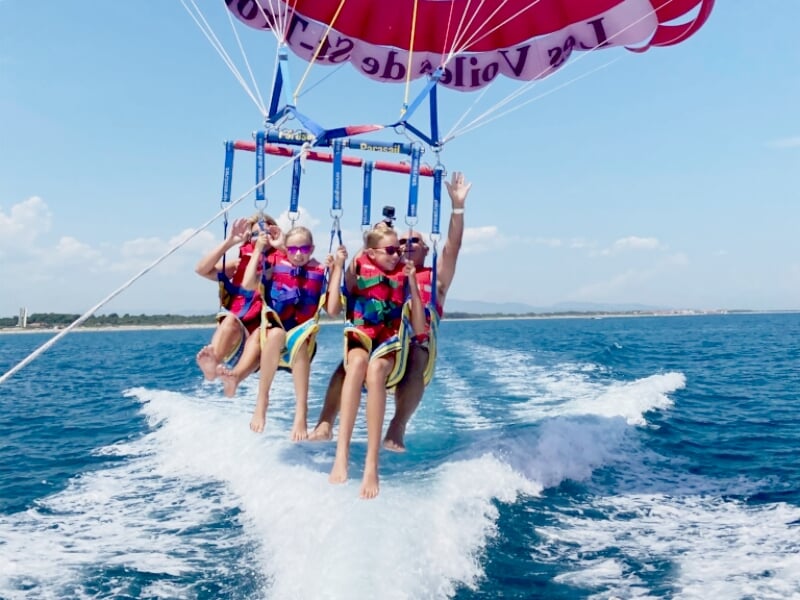 Quatre personnes en parachute ascensionnel suspendues au-dessus de l'eau, avec un bateau qui les tire en arrière.