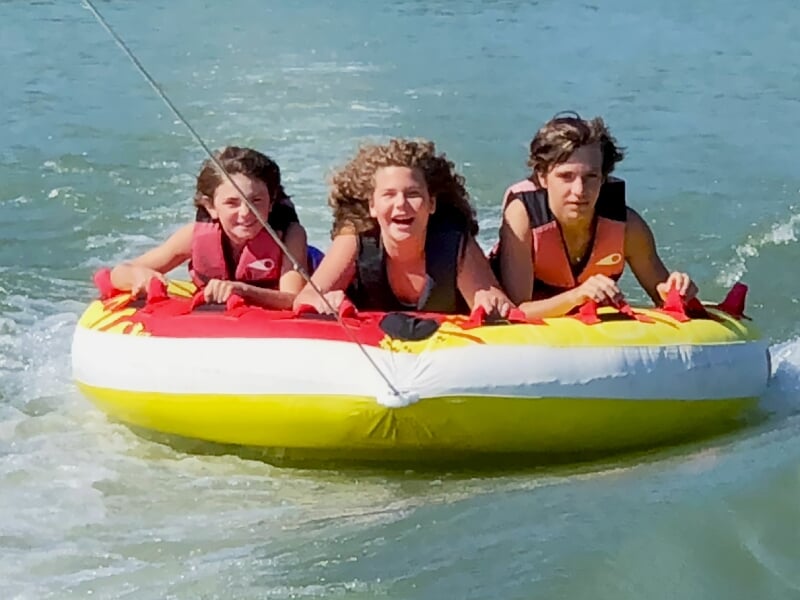 Trois enfants souriants sur une bouée tractée jaune et rouge glissant sur l'eau en mouvement.
