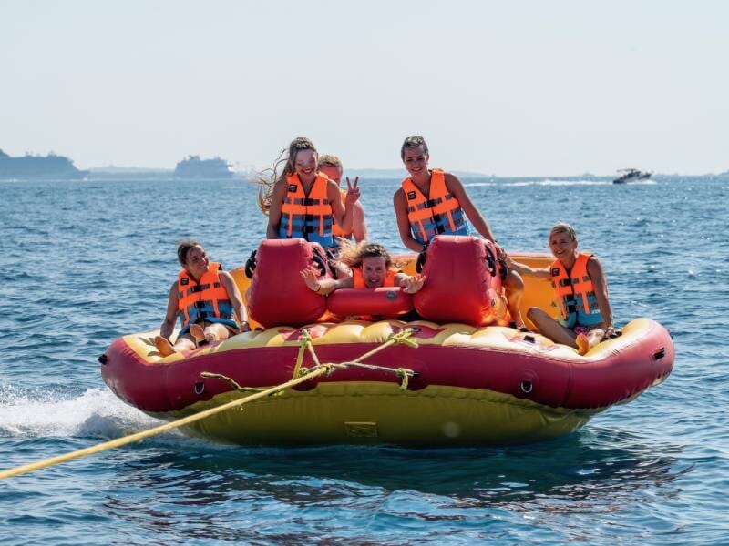 Cinq personnes portant des gilets de sauvetage orange sur une bouée tractée rouge et jaune en mer à Mandelieu-la-Napoule.