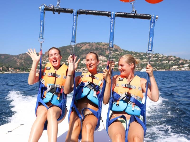 Trois femmes souriantes en gilets de sauvetage prêtes pour le parachute ascensionnel sur un bateau en mer à Mandelieu-la-Napoule.