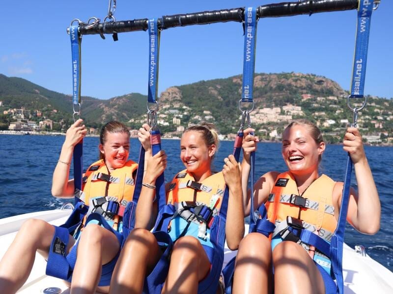 Trois femmes en harnais et gilets de sauvetage assises sur un bateau avant de décoller en parachute ascensionnel.