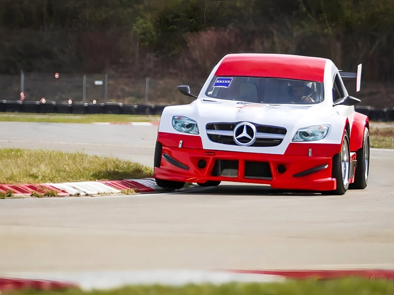 Voiture de course rouge et blanche avec logo Mercedes roulant sur une piste de circuit avec virage et bordure rouge et blanche.
