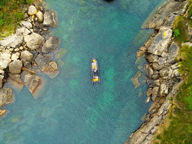 Vue aérienne d'un bateau dans une crique entourée de rochers et d'une végétation verte dense.