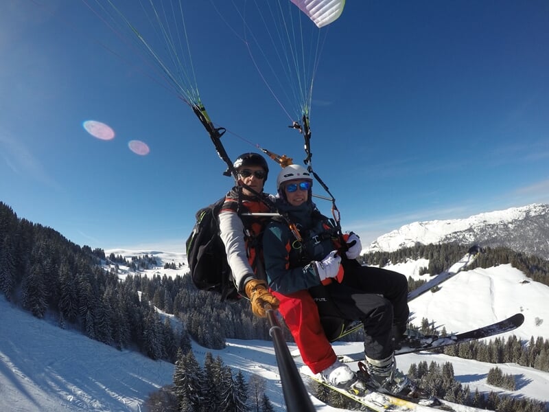 Parapente en tandem avec deux skieurs volant au-dessus d'une station de ski en hiver