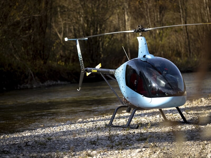 Hélicoptère bleu posé sur un terrain herbeux avec des arbres en arrière-plan