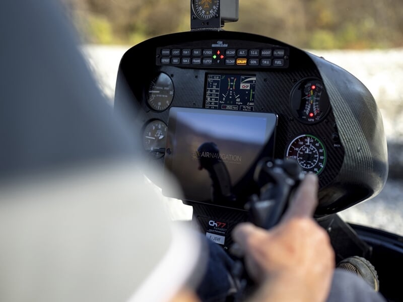 Hélicoptère bleu avec deux personnes à bord en vol au-dessus d'un paysage rural