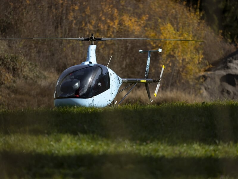 Hélicoptère bleu en vol au-dessus d'un paysage rural avec des champs et des arbres