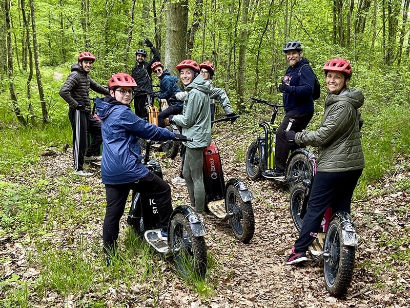 Les membres d'une famille en trottinettes électriques tout-terrain posent devant leurs engins au milieu des bois.
